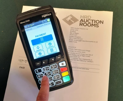 Ingenico Move/3500 payment terminal on a printed HRD Auction Rooms document; screen shows Payment Main Menu with a finger on the keypad.